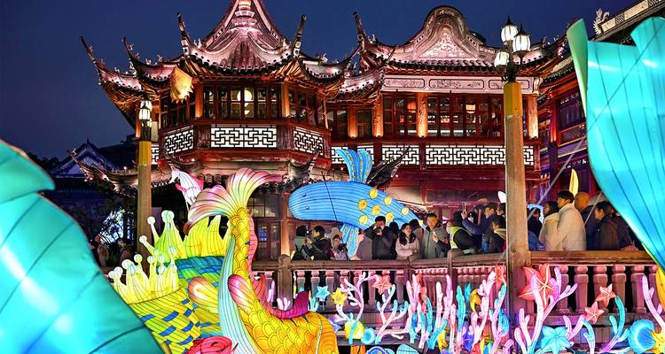 Ein beleuchteter traditioneller Pavillon und farbenfrohe Laternenplastiken ziehen abends Besucher während eines lebendigen Lichtfestivals an.