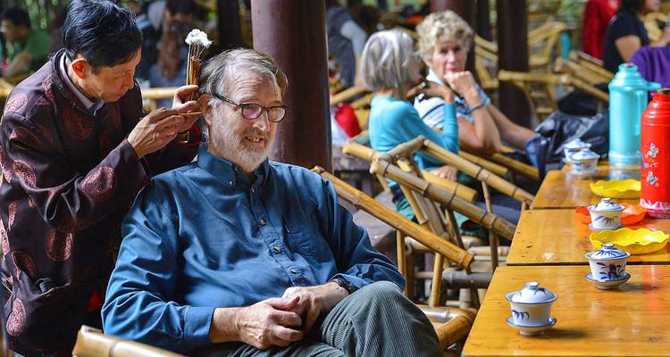 Local ear cleaner tending to a seated visitor in Chengdu’s traditional teahouse garden.