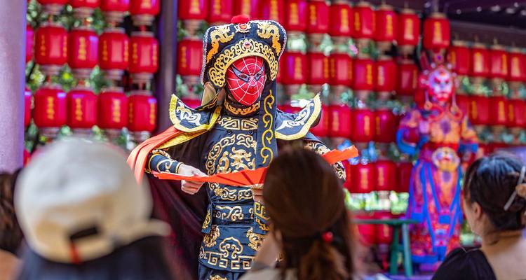 Sichuan opera performer in ornate mask and costume executing face-changing act before an audience.
