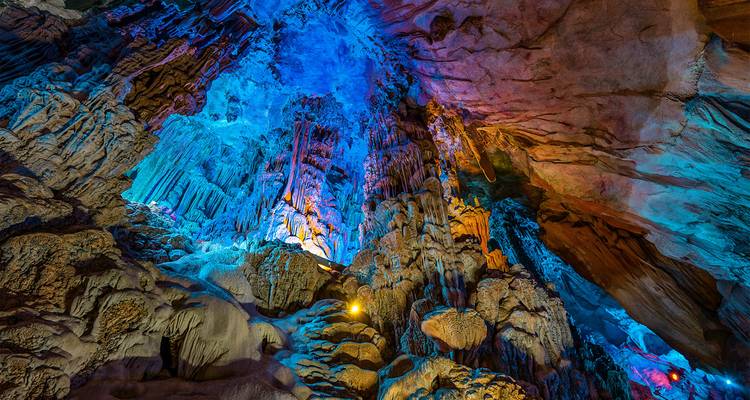 Spektakuläre Stalaktiten, die mit blauen und magentafarbenen Lichtern in einer riesigen Kalksteinhöhle beleuchtet werden.