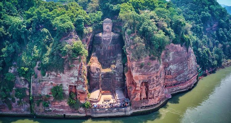 Aerial view of the colossal Leshan Giant Buddha carved into a red cliff beside a winding river.