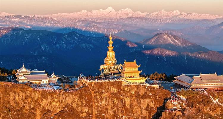 Golden summit statue and temples of Mount Emei glow at sunrise with snow-capped peaks in the distance.