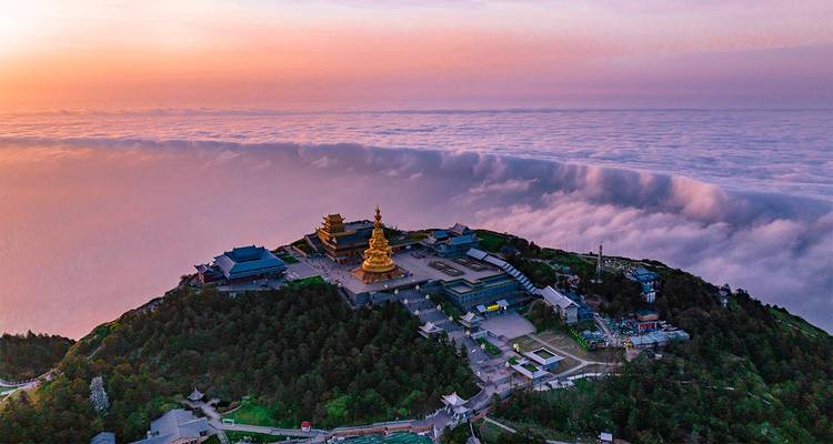 Dramatic aerial of Mount Emei’s golden summit temple complex rising above a sea of clouds at dawn.