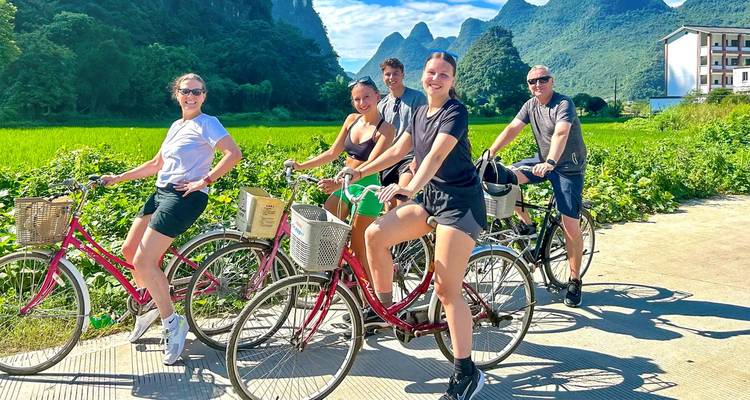 Grupo sonriente de ciclistas posando con campos de arroz y picos de piedra caliza afilados detrás de ellos