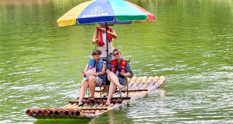 Pareja sentada en una pequeña balsa de bambú con sombrilla colorida deslizándose sobre el agua verde del río