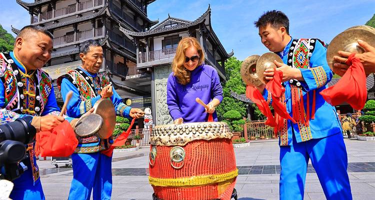 Tourist joins local performers in bright ethnic costumes beating a large ceremonial drum in a temple courtyard