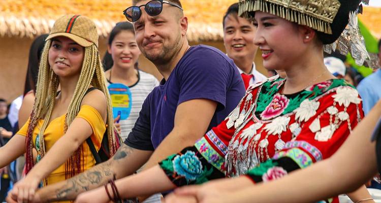 Tourists and locals join hands dancing in colourful ethnic costumes at a village festival