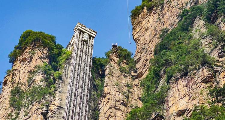 Tall Bailong Elevator and adjacent bungee jump platform set against sheer cliff walls under clear sky