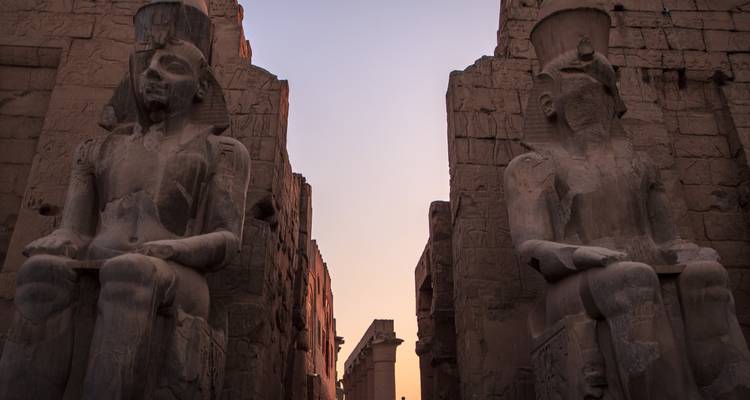 Vue du coucher de soleil sur le temple de Louxor avec des statues imposantes.