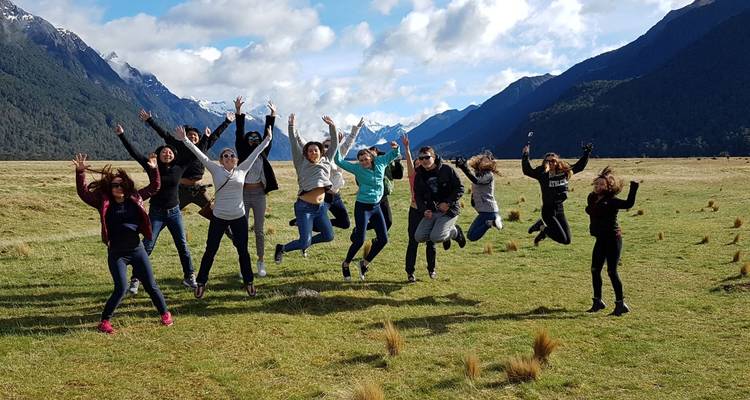 Gente saltando en un campo cubierto de hierba con montañas al fondo.