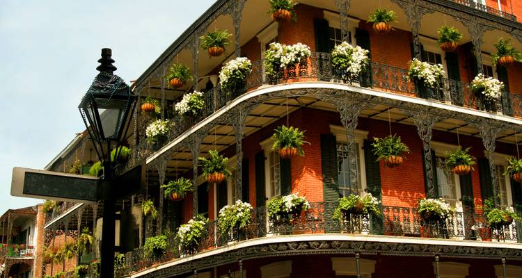Historic red-brick French Quarter building adorned with ornate wrought-iron balconies filled with hanging plants and flowers.