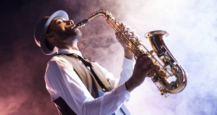Stylish saxophonist passionately playing on a smoky stage with dramatic colored lighting.