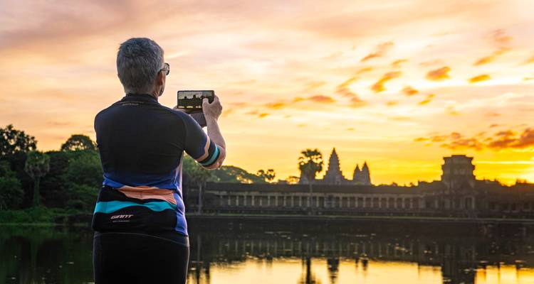 Person taking a photo of a temple against a sunset sky backdrop.