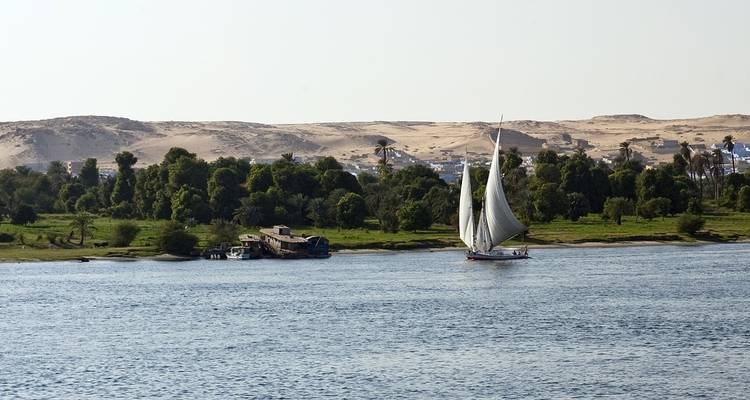 Segelboot auf dem Nil mit einer Wüstenlandschaft im Hintergrund.
