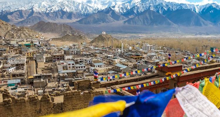 Paysage urbain avec des drapeaux de prière colorés sur fond de montagnes majestueuses.