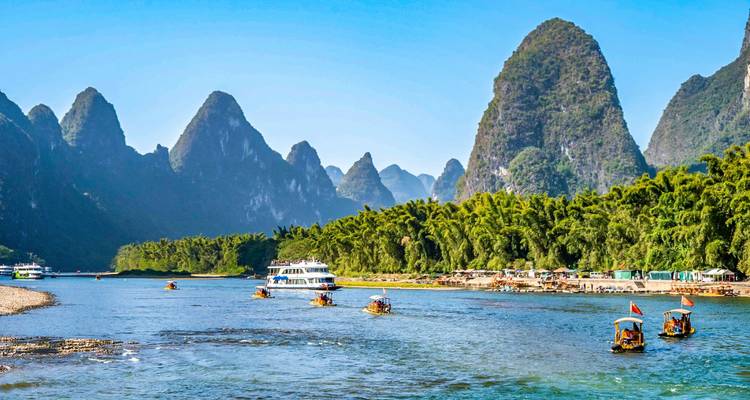 Kalksteenbergen langs de Li-rivier met bamboevlotten en cruiseschepen op een zonnige dag