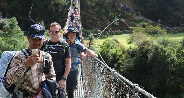 Personas cruzando un puente colgante en una zona boscosa.