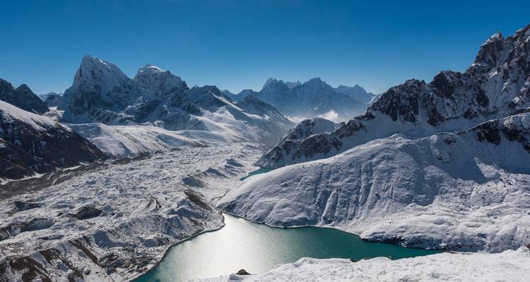 Snow-covered mountains with a lake below, under a clear blue sky.