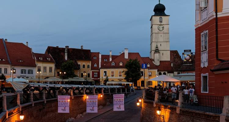 Eine lebhafte Straße mit einem Uhrenturm und Sitzgelegenheiten am Abend.