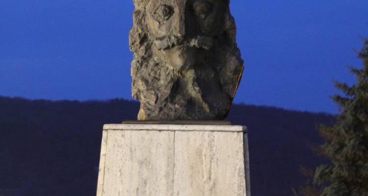 A stone bust on a pedestal at night.