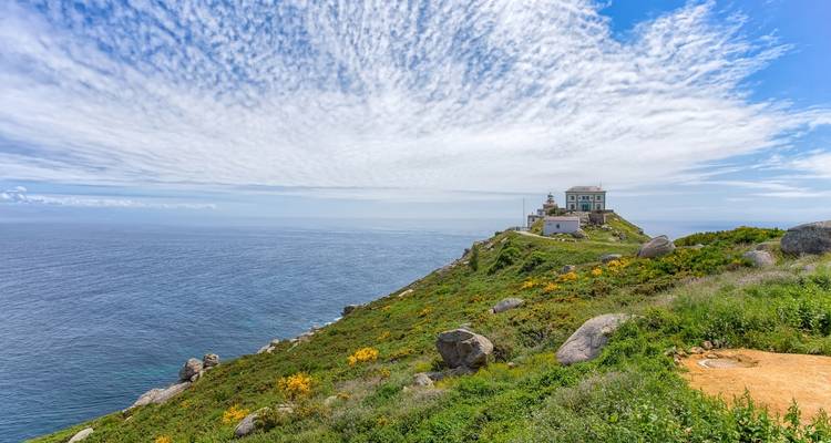 Faro de Cabo Fisterra con vegetación y fondo oceánico.