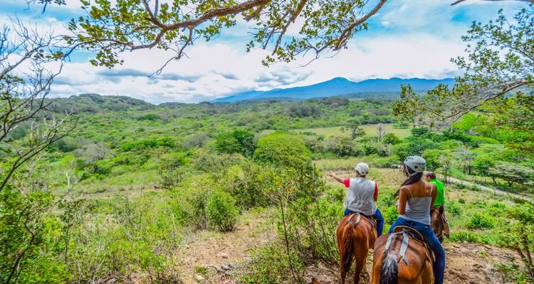 Gente montando a caballo con un paisaje montañoso de fondo.