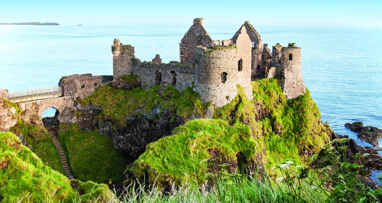 Ruins of a cliff-top stone castle overlooking a rugged coast and blue sea.