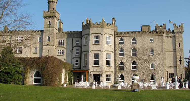 Historic grey-stone castle hotel with manicured lawn and outdoor seating.