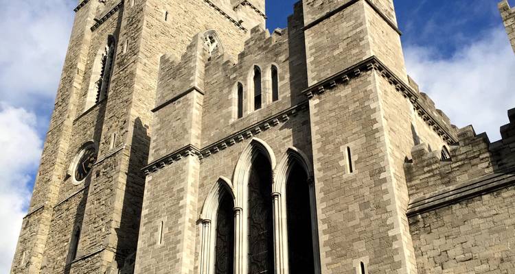 Stone Gothic cathedral tower rising against a partly cloudy sky in Dublin.