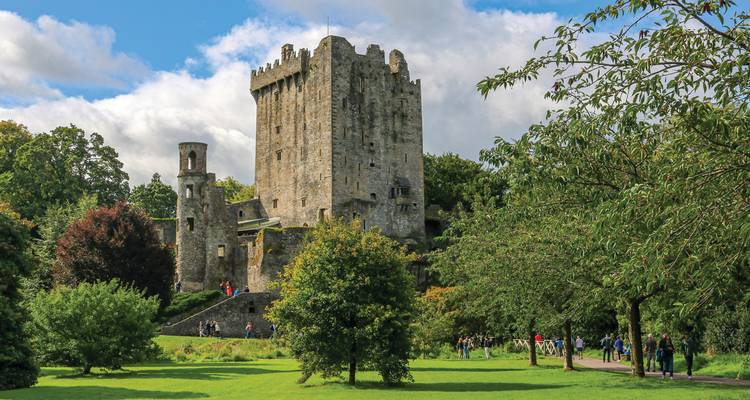 Medieval Blarney Castle rising above lush green gardens and visitors on a sunny day