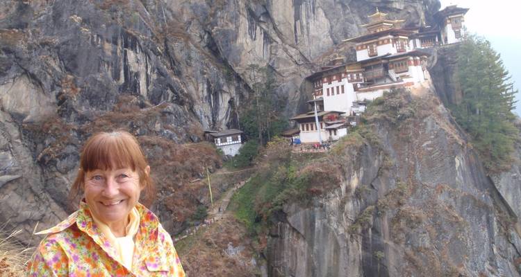 Glimlachende vrouwelijke reiziger met Bhutans beroemde Tiger's Nest klooster hoog op een klif achter haar.