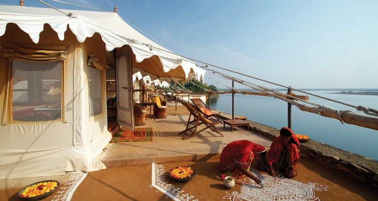 Zwei Personen schmücken den Boden in der Nähe von luxuriösen Zelten mit Blick auf einen See.