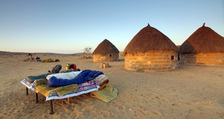 Traditionelle strohgedeckte Hütten mit einem Schlafplatz im Vordergrund.