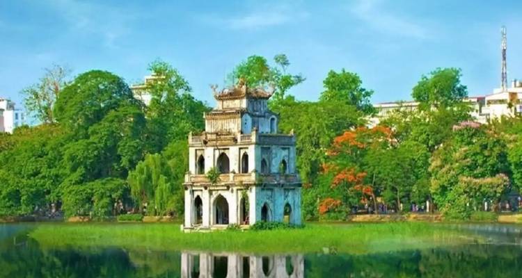Turtle Tower rises from the centre of Hoan Kiem Lake surrounded by lush trees reflected in the still water.