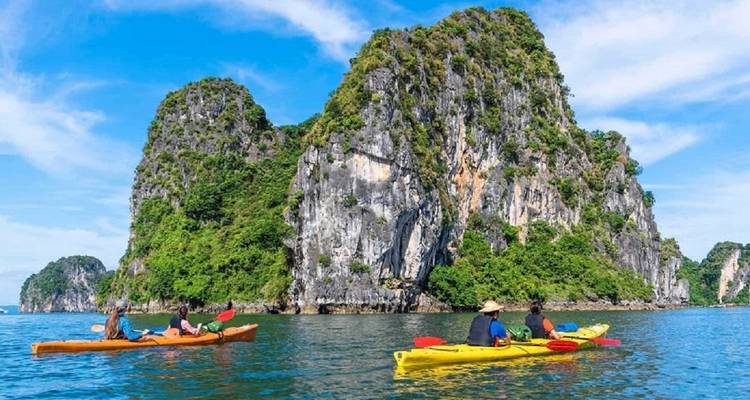 Two colourful kayaks with travellers paddle past a steep, jungle-covered limestone island