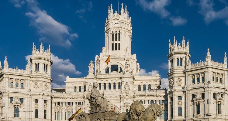 Sunny view of the ornate white Palacio de Cibeles with the Cibeles Fountain lions in front, set against a deep blue sky.