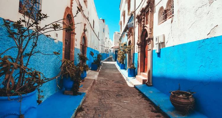 Enge Gasse in lebendigen Blau- und Weißtönen gestrichen, typisch für Chefchaouen unter starkem Sonnenlicht.