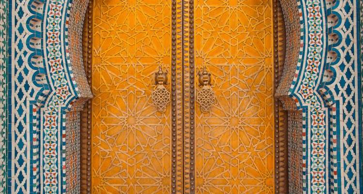 Close-up of a vibrant orange Moroccan door framed by intricate blue and white mosaic tiles.
