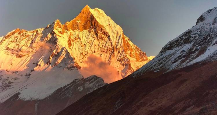 Fiery sunrise lights up the sheer face of Annapurna amid swirling morning clouds.