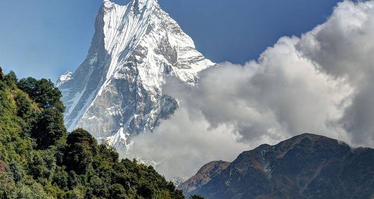 Dramatische, met sneeuw bedekte top van de Machapuchare torent boven groene bosrijke voethellingen en wolken uit
