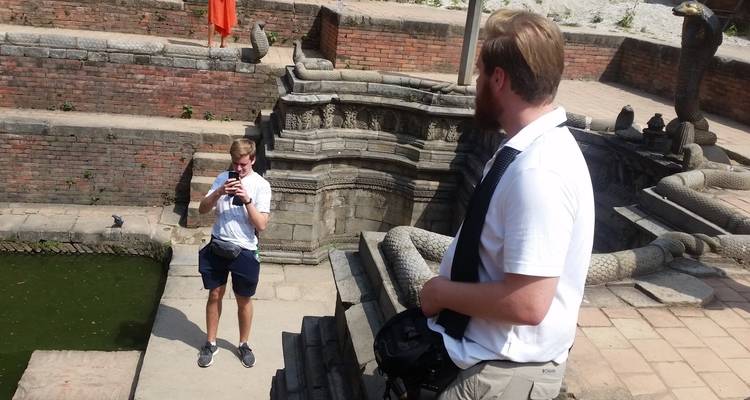 Tourists photographing each other beside an ancient stone serpent fountain