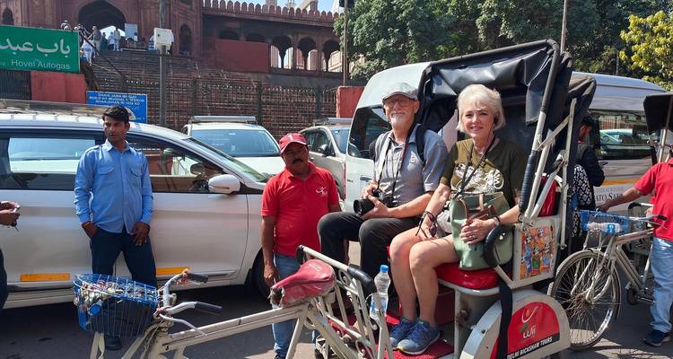 A couple on a rickshaw in a busy street in front of a historical building.