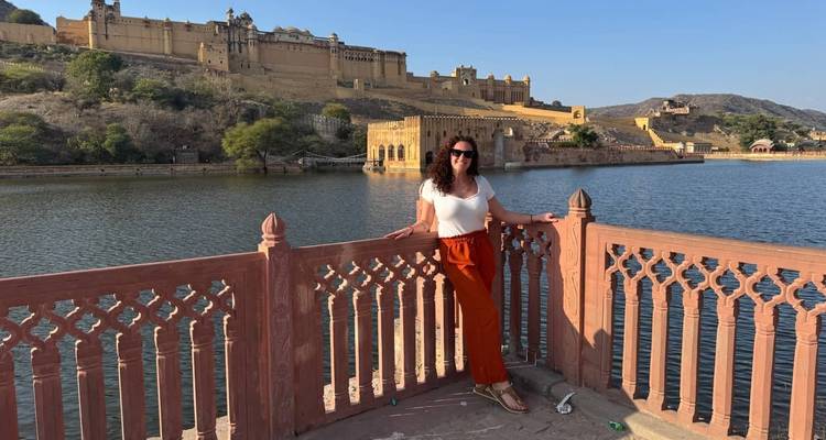 A woman posing by a water body with a fort in the background.