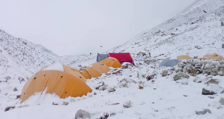Camp enneigé avec des tentes dans une zone montagneuse rocheuse.