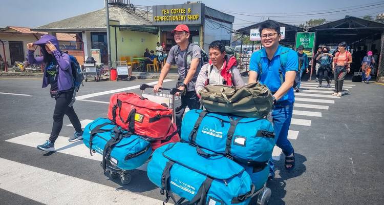 Des trekkeurs poussant des chariots à bagages avec des sacs de voyage à travers un passage pour piétons d'aéroport au Népal.