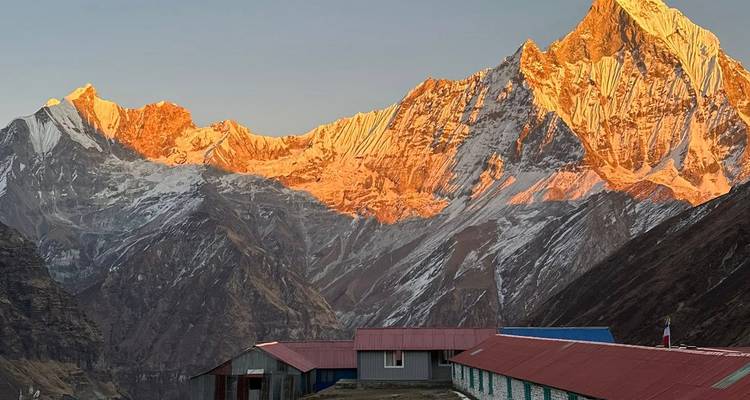 Gouden alpenglow verlicht de Machhapuchhre-top boven berghutten bij zonsopgang.