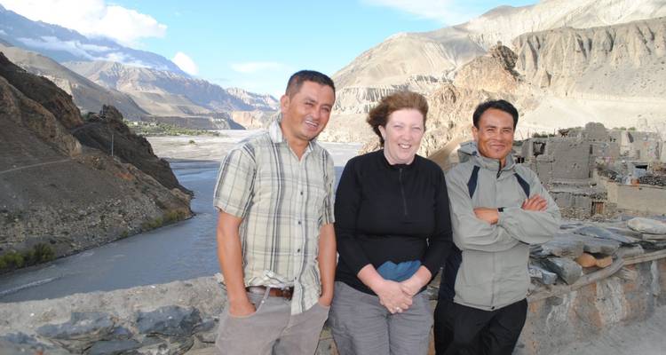 Drie reizigers lachen tegen een dramatische achtergrond van bergen en een rivierdal in Mustang.