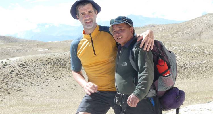 Twee trekkers in hooggebergte terrein poseren vrolijk met rugzakken tussen aride glooiende heuvels.