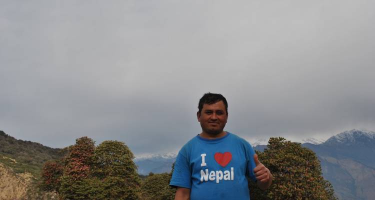 Lachende man met een 'I ♥ Nepal' T-shirt die een duim omhoog geeft met mistige bergen op de achtergrond