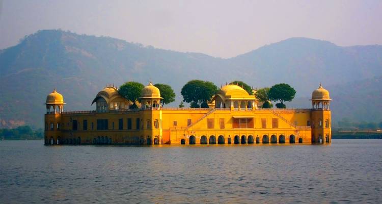 Jal Mahal steht inmitten eines Sees mit Hügeln im Hintergrund.